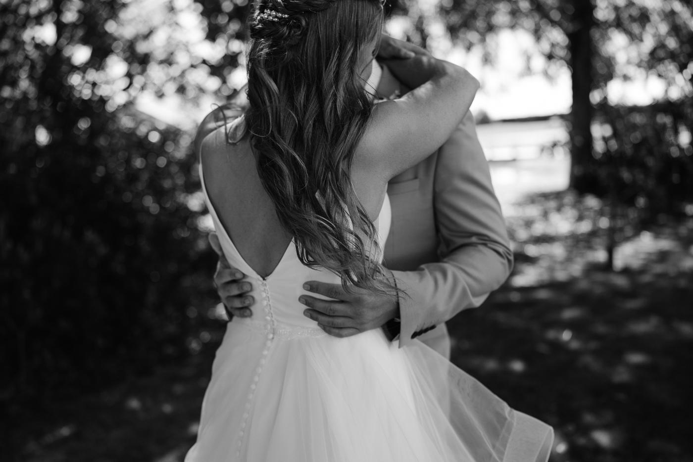 A bride and groom embracing in black and white, her veil moving
