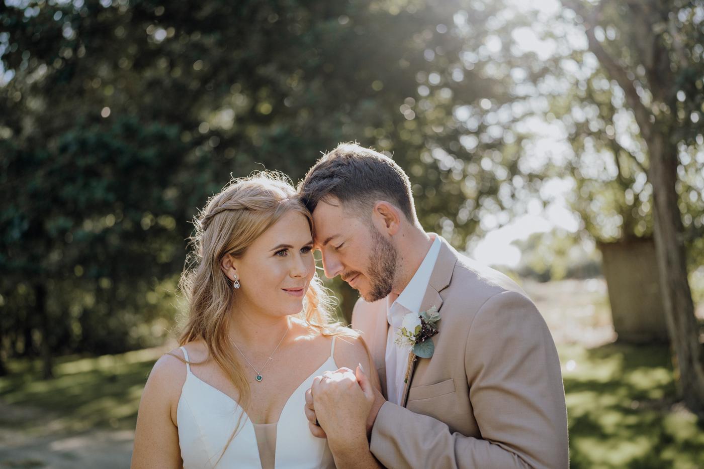 A bride and groom with foreheads together in dappled light