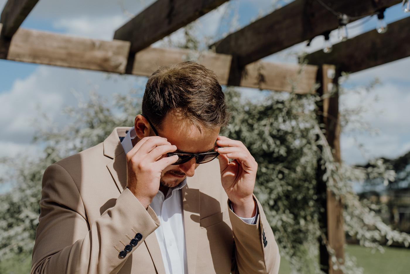 A groom grinning as he puts on his sunglasses