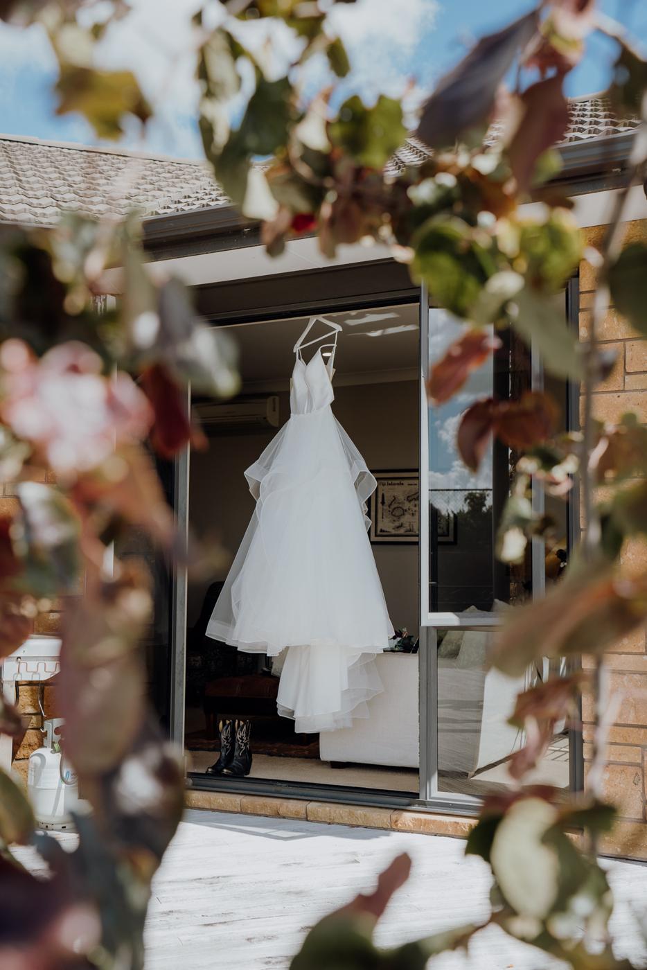 A wedding dress hanging in the window of a rustic building