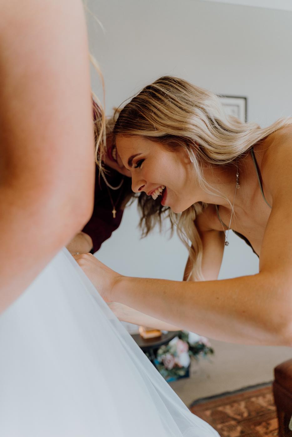 A bride laughing as her dress is adjusted