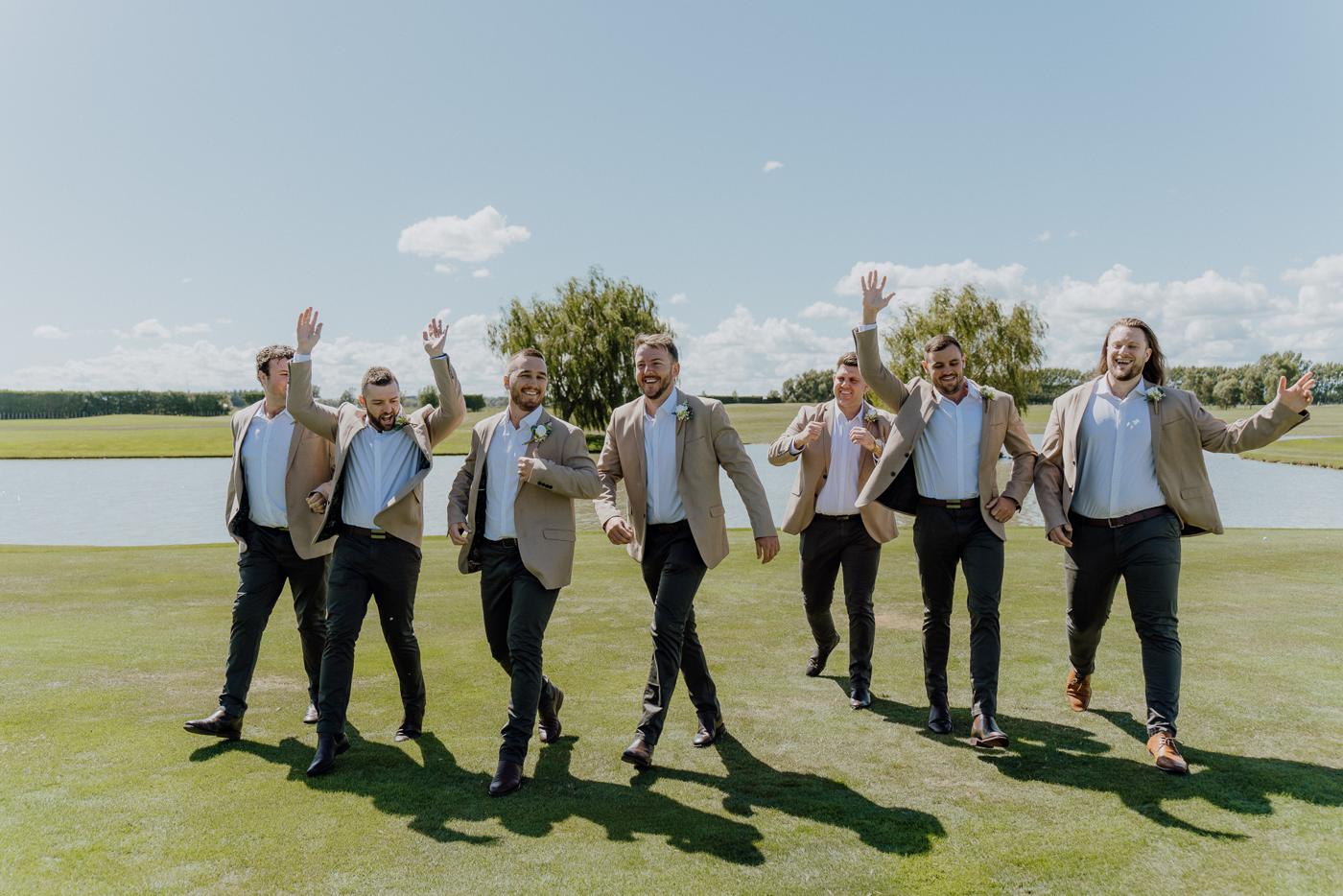 Groom and groomsmen walking and cheering across a lawn