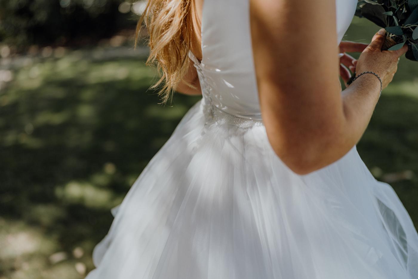 A bride's dress in dappled light with hands holding her bouquet