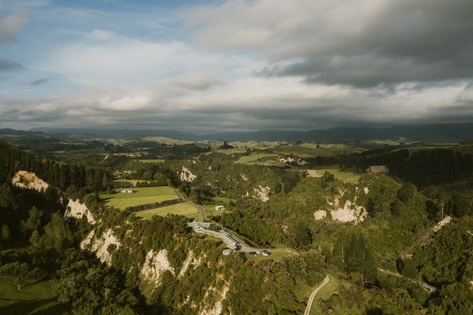 An aerial view of green farmland and river valley under a stormy sky