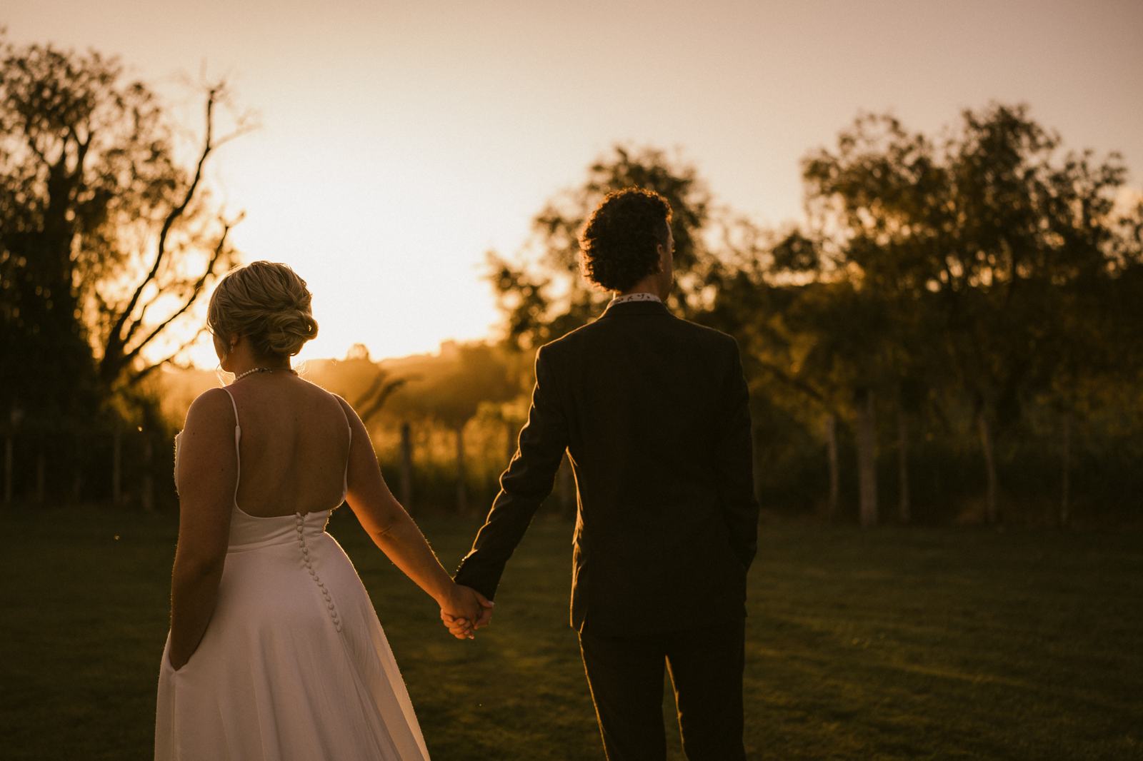 A couple walking hand in hand into a low golden sunset between the trees