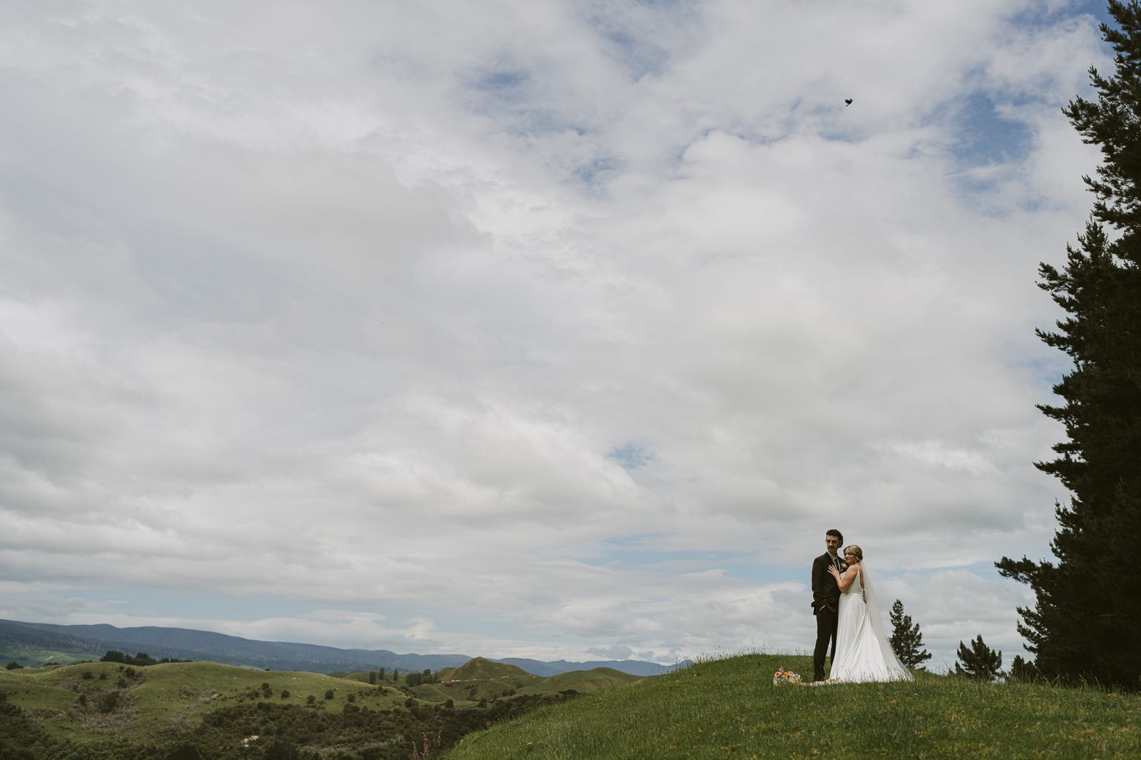 A couple small on a green hill under a wide sky