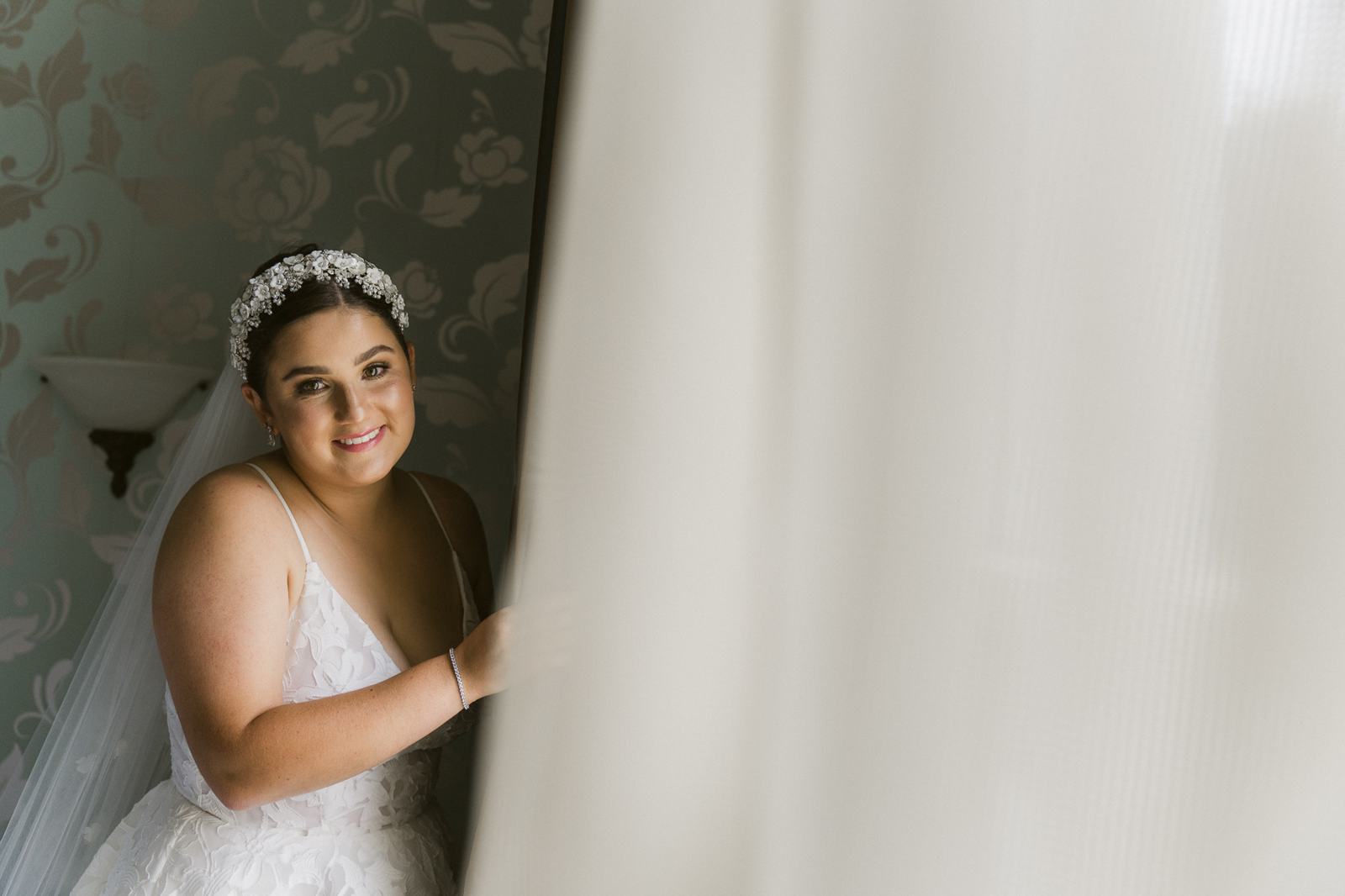 A bride smiling beside a sheer curtain