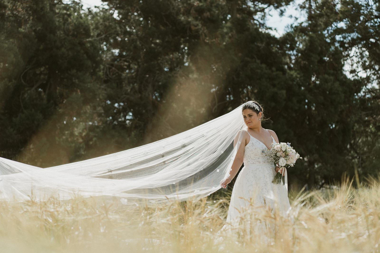 A bride in a wheat field, her long veil lifting in the wind