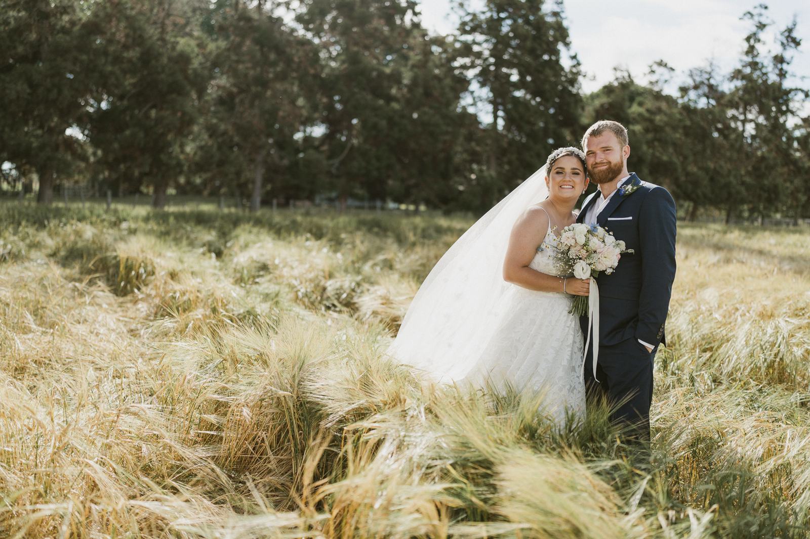 A bride and groom standing close in long golden grass