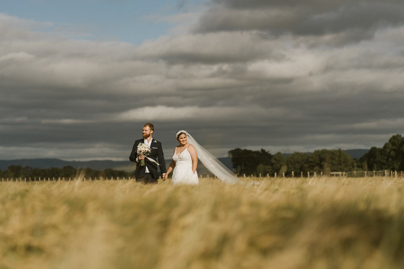 A couple small in a wide golden field under cloud