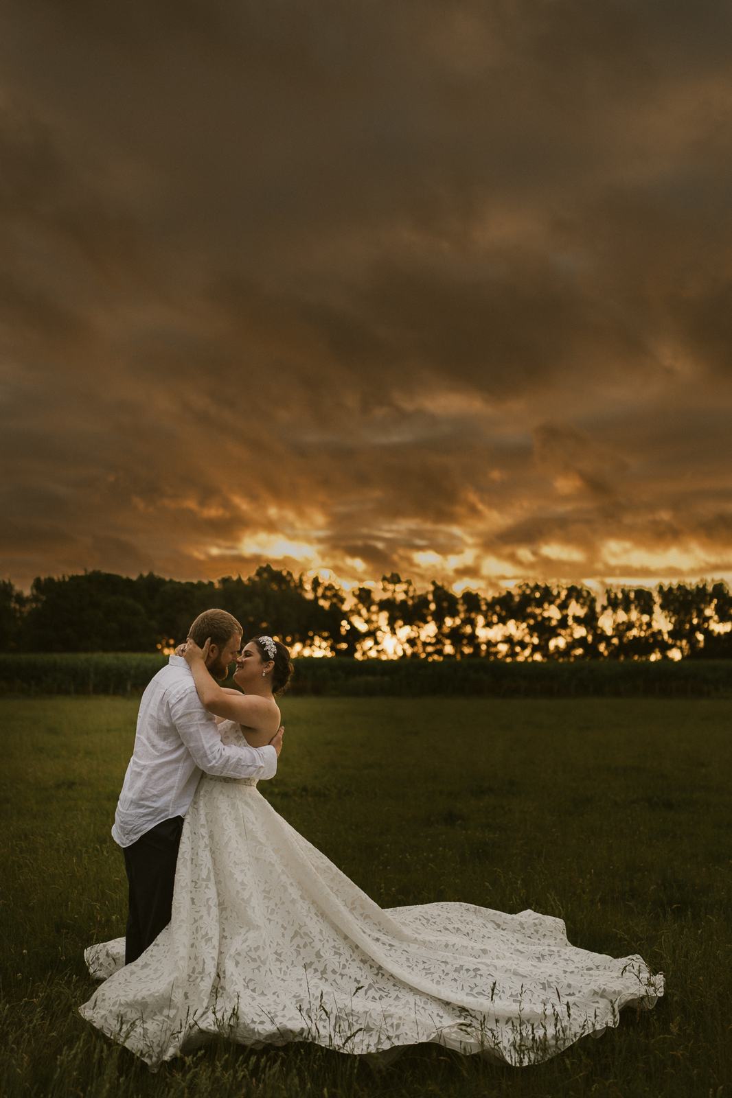 A bride embracing her groom in a field under a dramatic orange sky