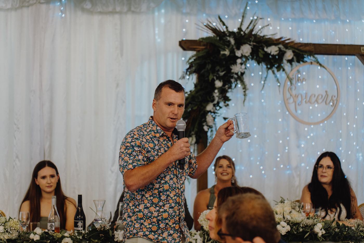 A groomsman giving a speech beside a floral arch