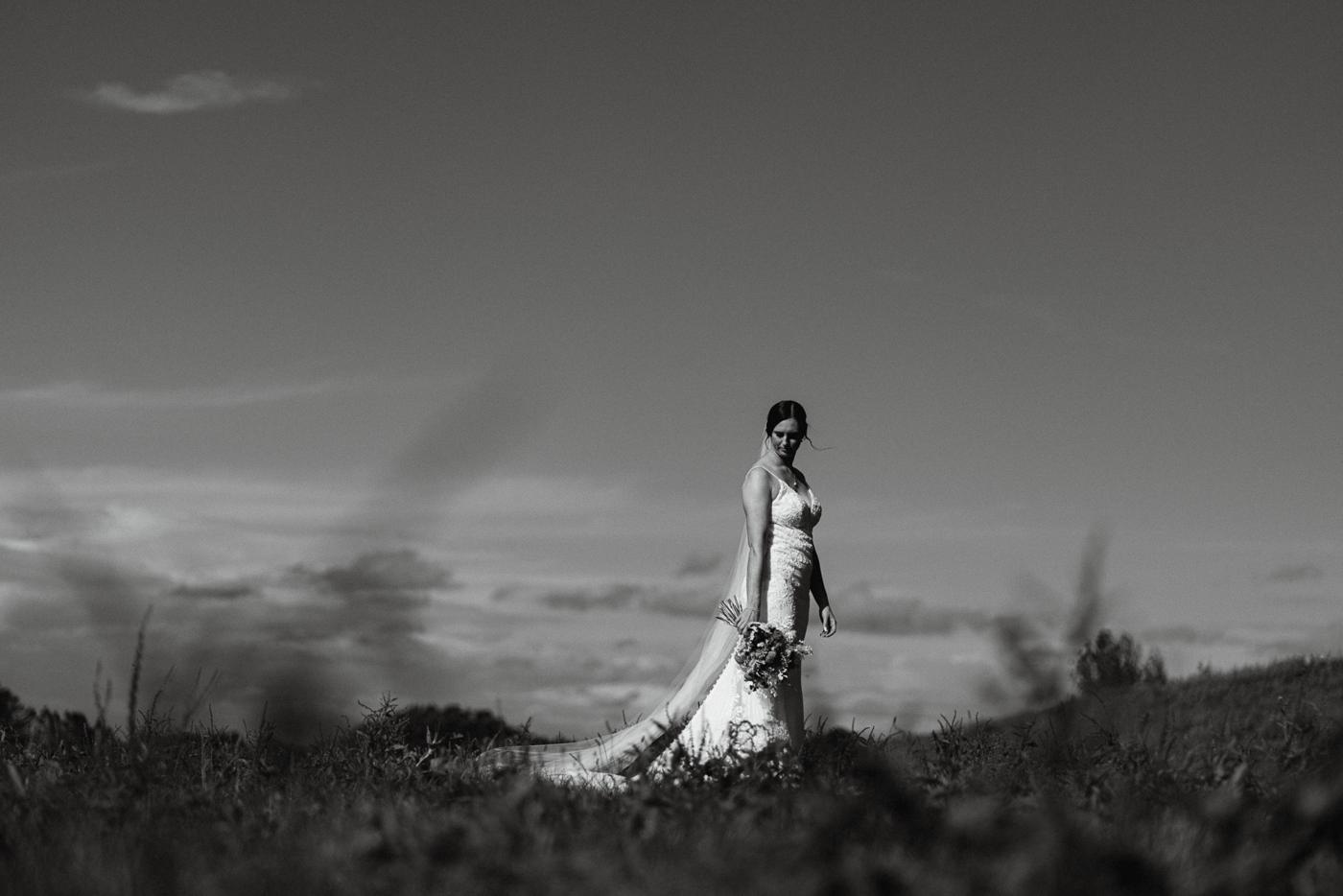 A bride in black and white on a hill with the sky behind