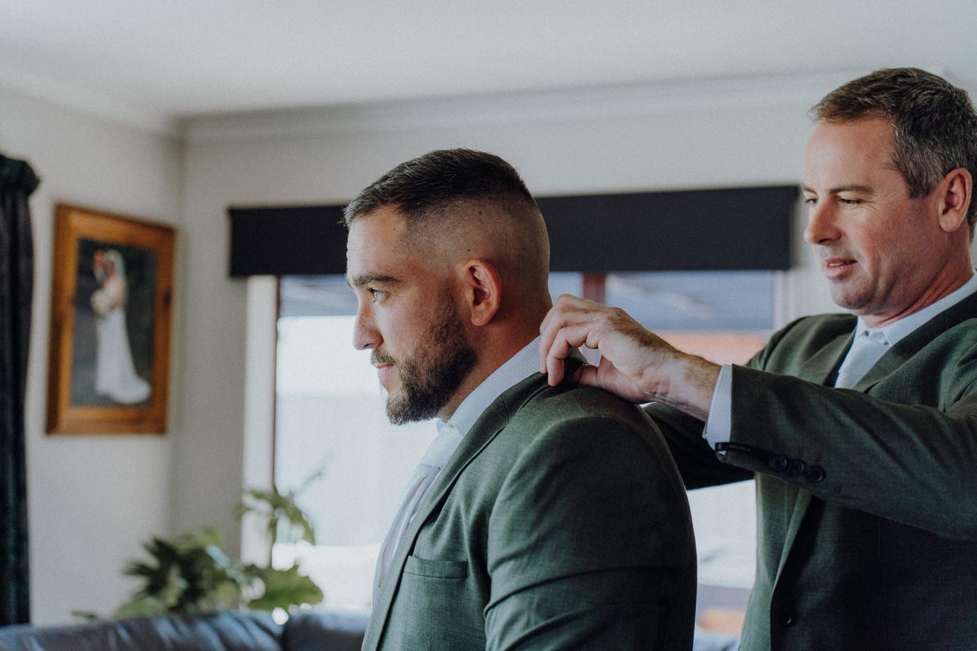 A groom being helped with his jacket by a friend