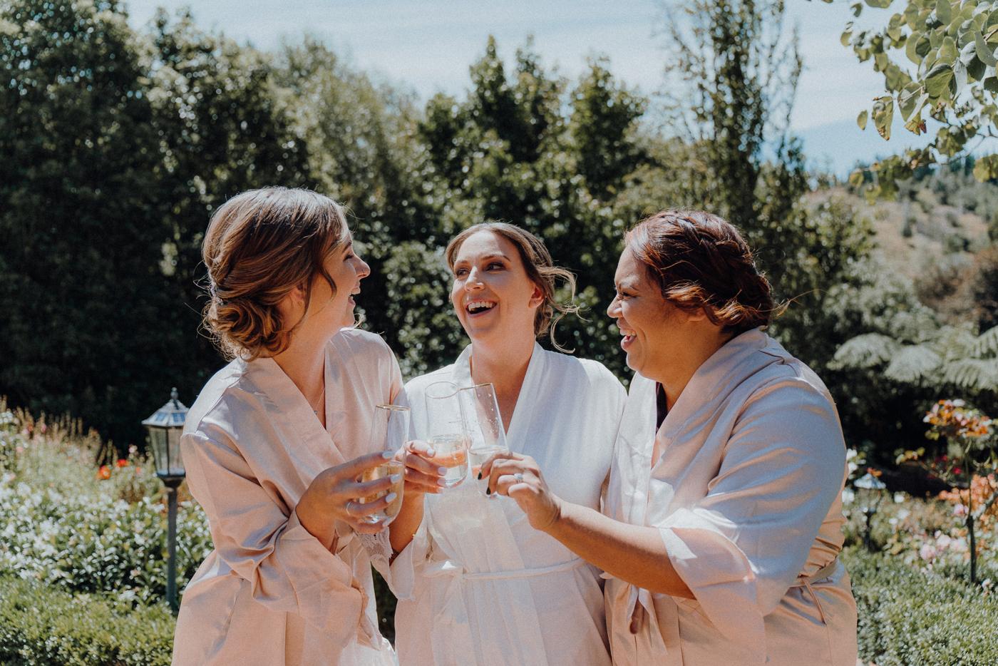 Three women in robes laughing with glasses in hand
