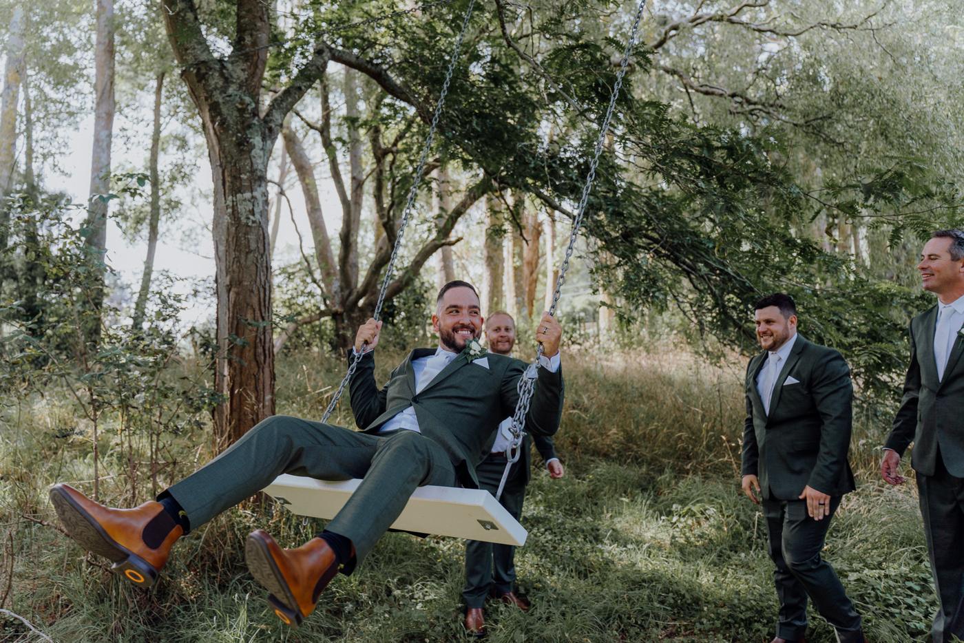 A groomsman on a swing among the trees while the bridal party watches