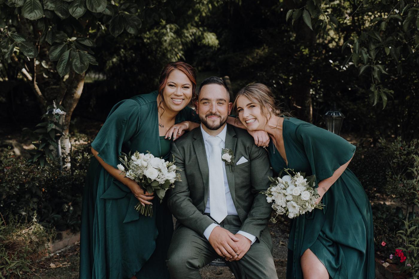A groom with two bridesmaids in green, smiling