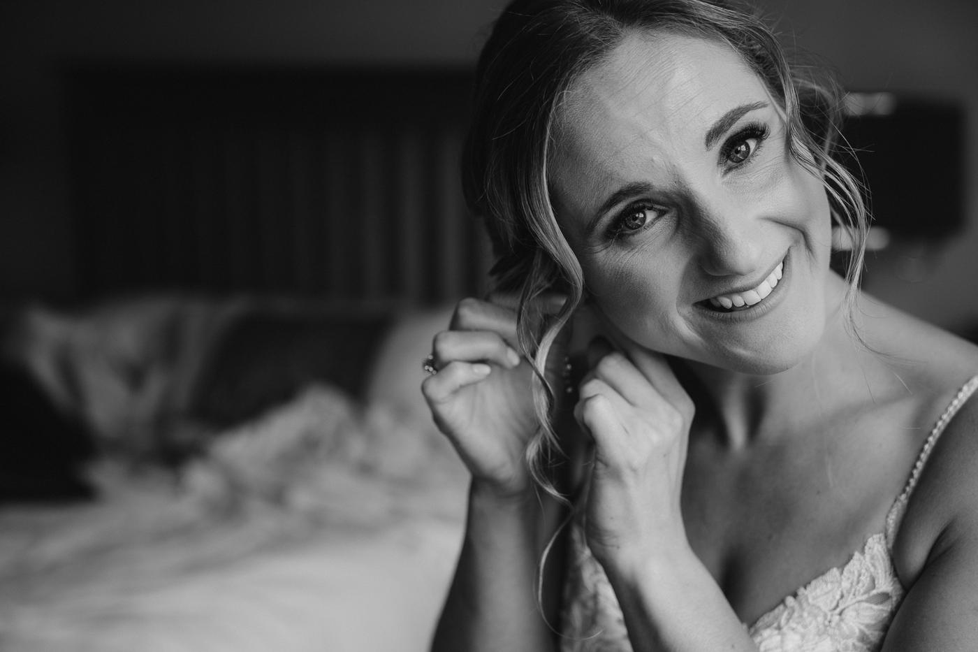A bride smiling while putting in an earring, in black and white