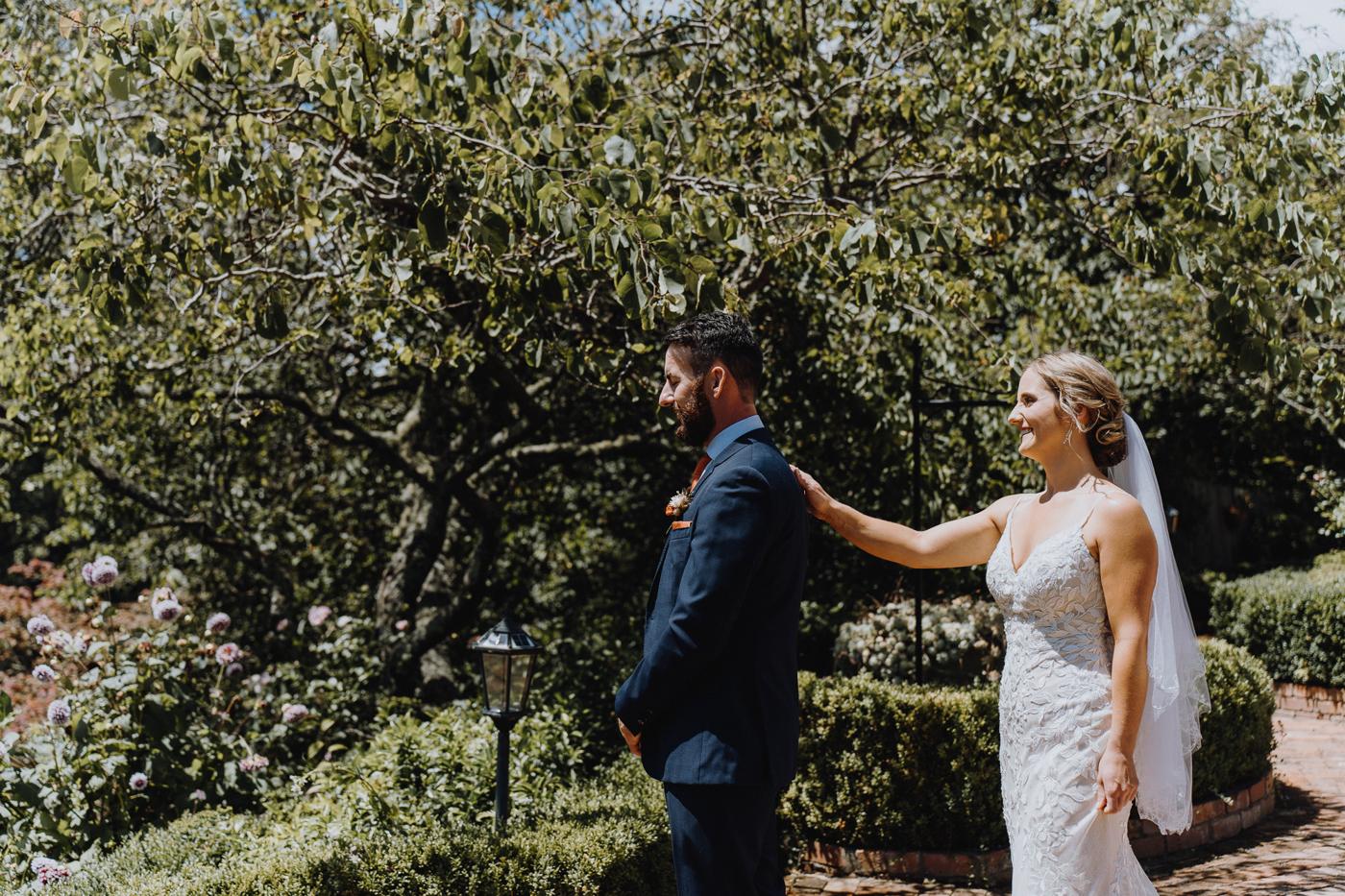 A groom and bride in a garden first look, her hand on his shoulder