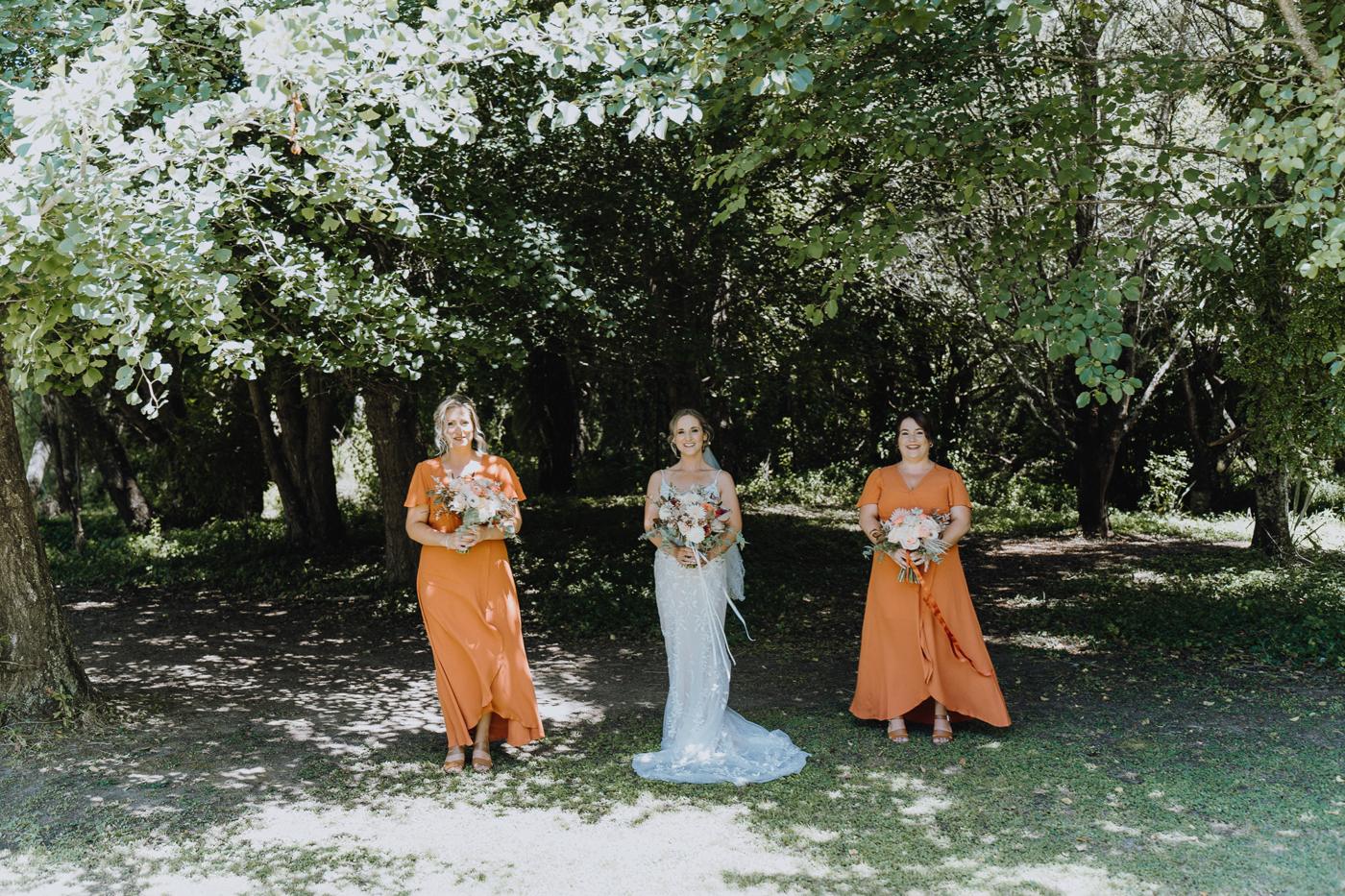 Bridesmaids in orange dresses with the bride in a leafy garden