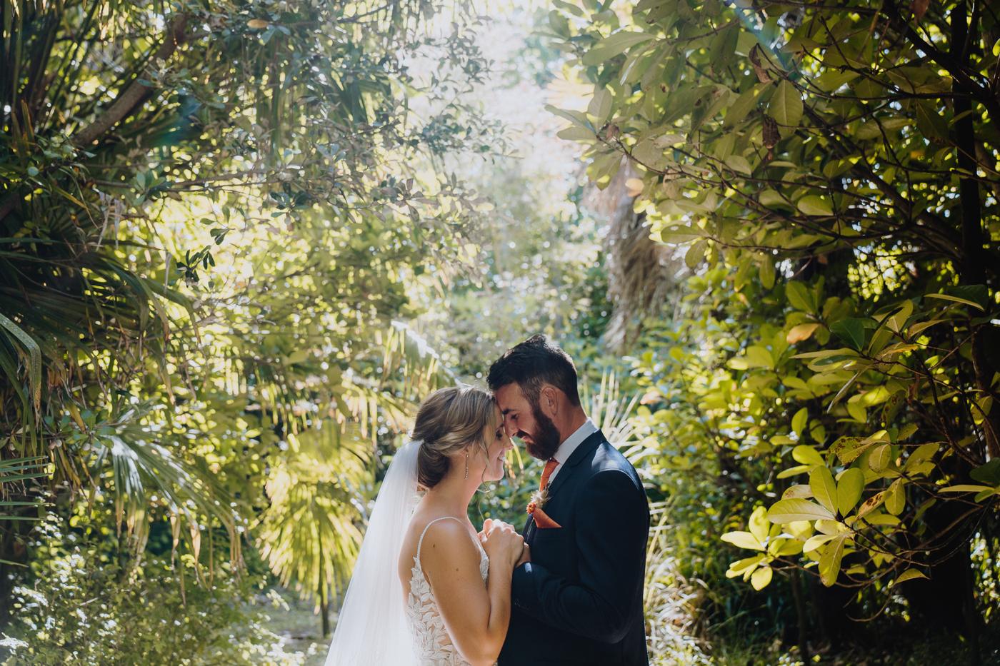 A bride and groom with their foreheads together in a leafy garden