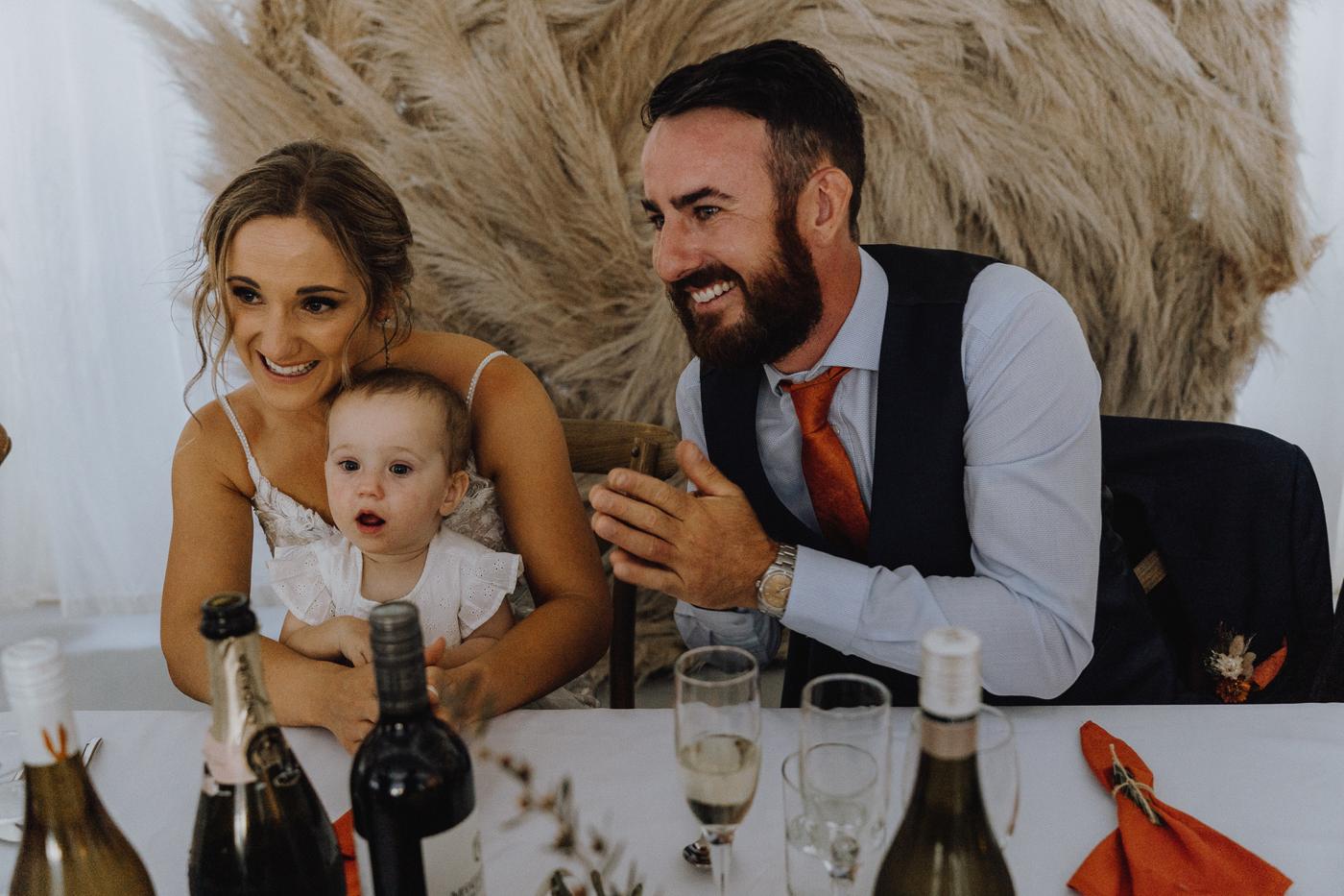 A bride and groom laughing at the head table with their baby