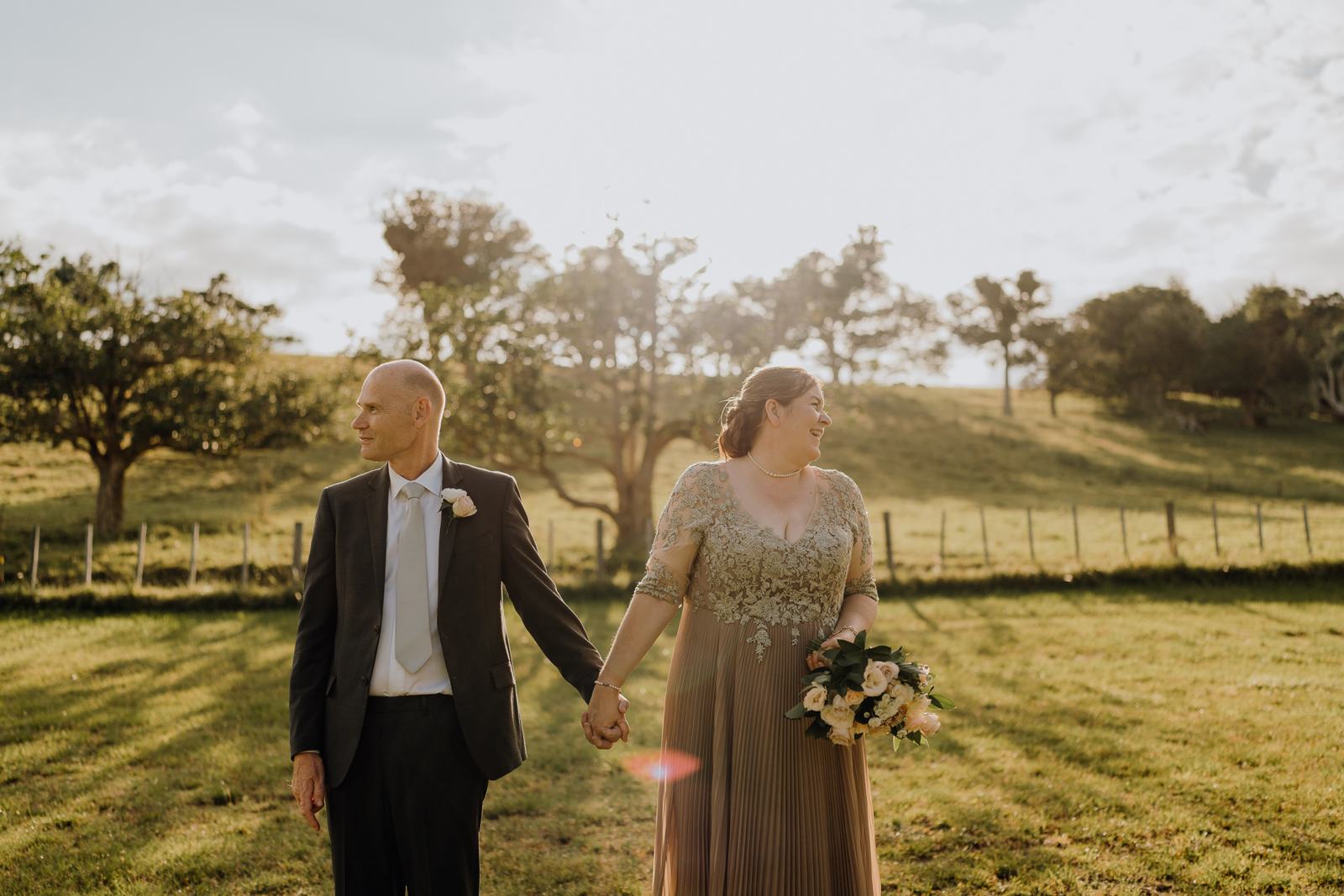 A couple walking hand in hand across a golden paddock