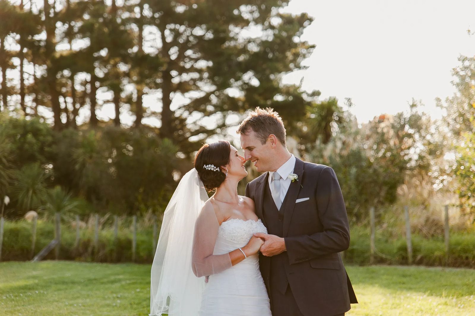 A bride and groom touching foreheads on a sunlit lawn