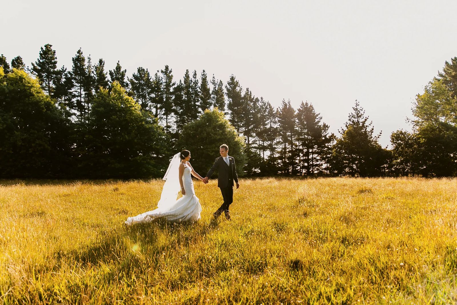 A bride in a flowing gown walking through a golden field with her groom