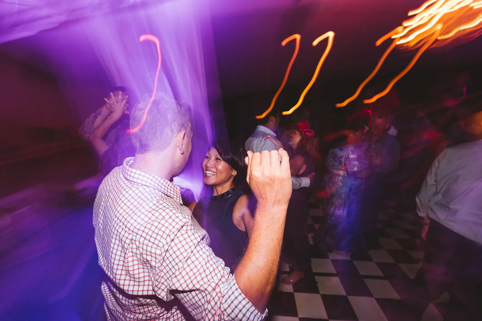Guests dancing under purple party lights, blurred with movement