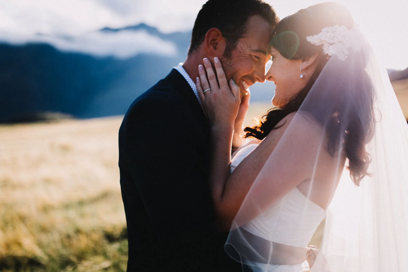 A couple holding each other close, foreheads touching, with mountains behind