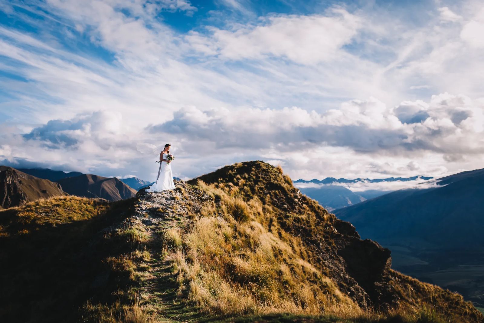 A couple standing tiny on a mountain ridge under a huge sky