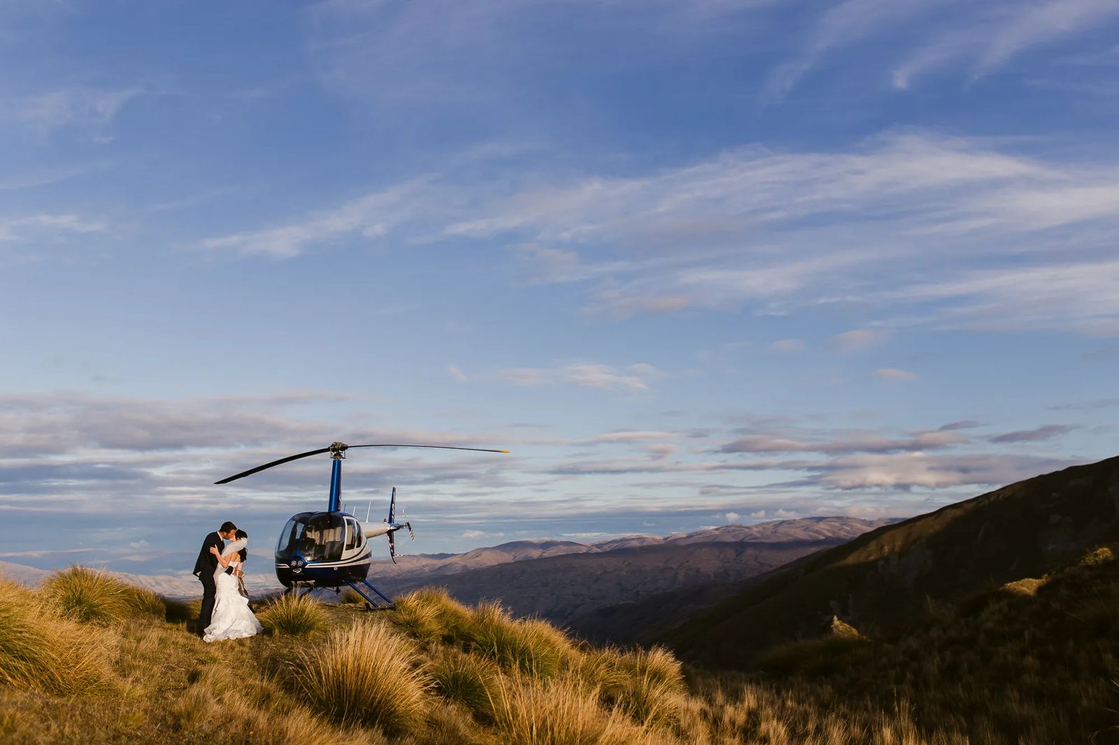 A couple beside a helicopter on a golden mountainside