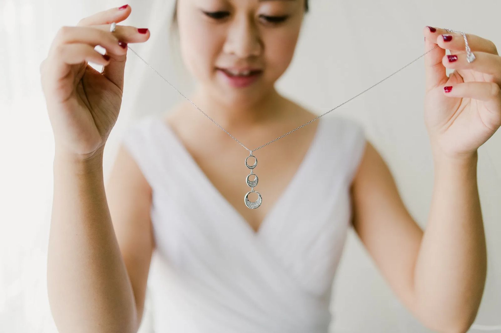 A bride adjusting a pendant necklace as she gets ready