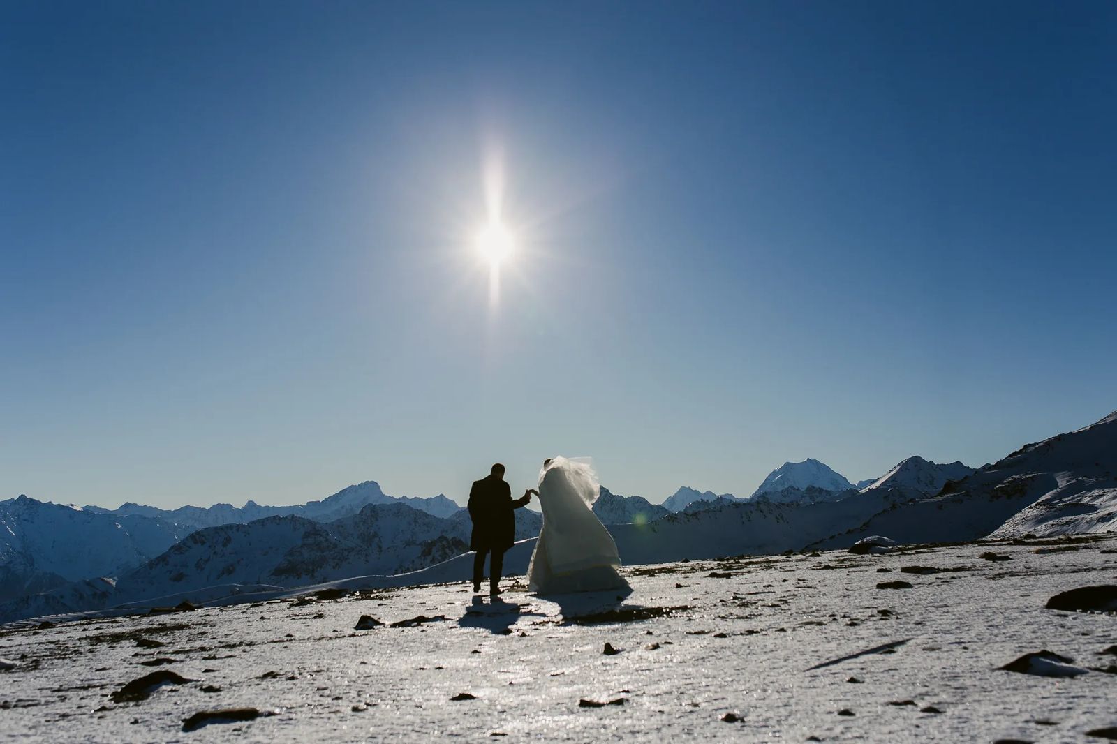 A couple standing on a snowy mountaintop under a bright sun