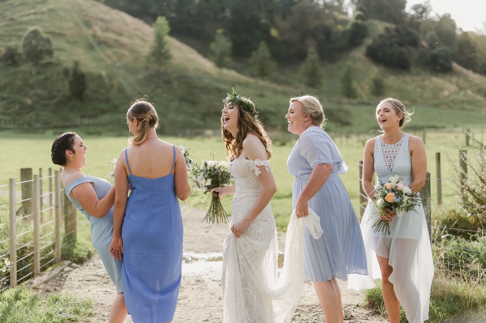 Bridesmaids laughing together on a grassy hill