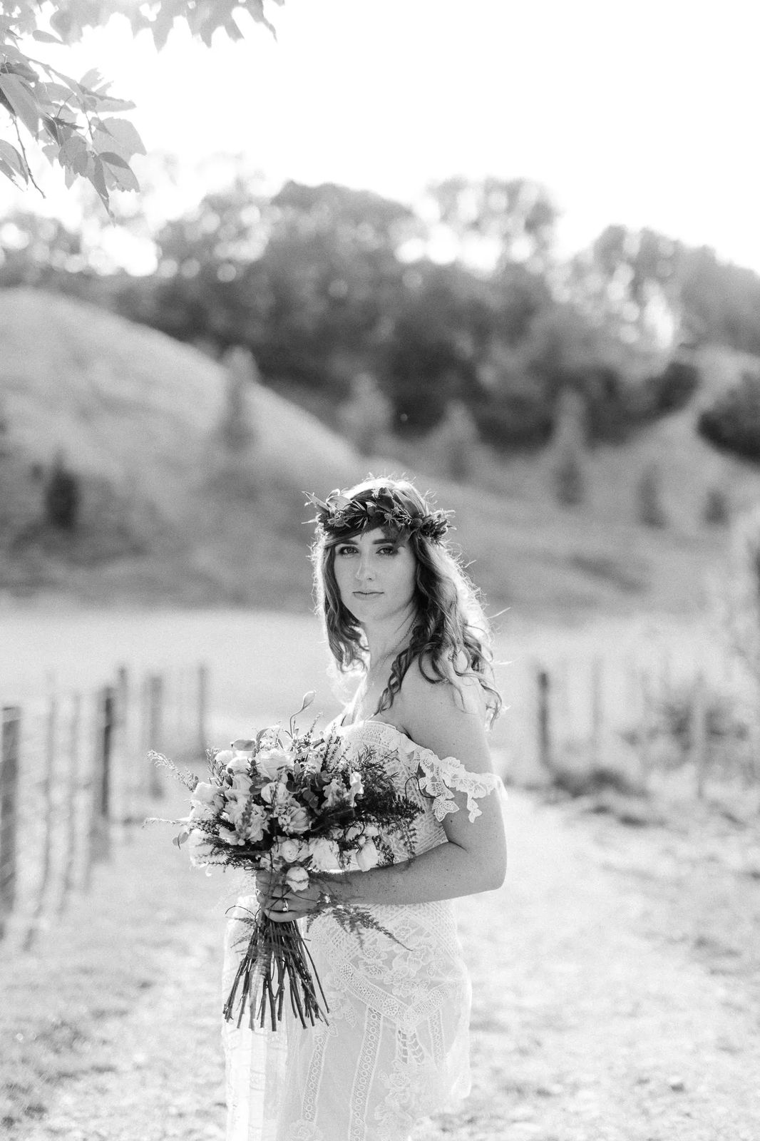 A bride in a flower crown with a bouquet on a country path, black and white