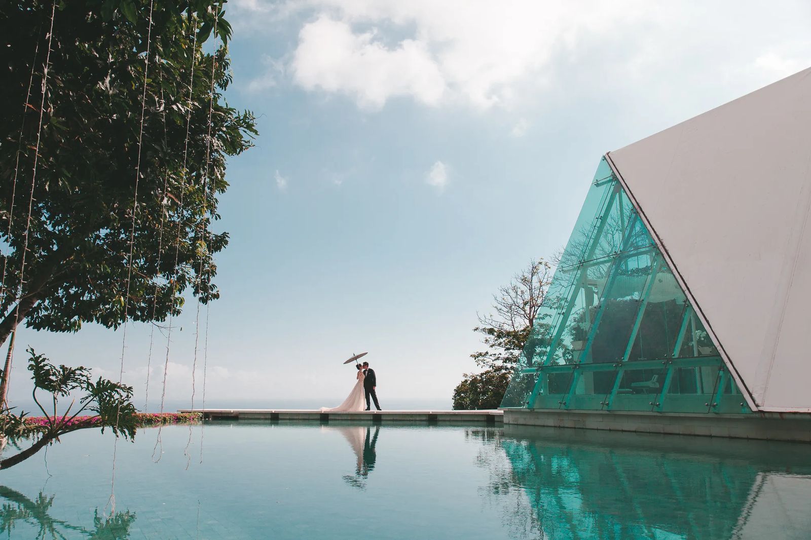 A couple beside a reflecting pool with a glass pyramid building