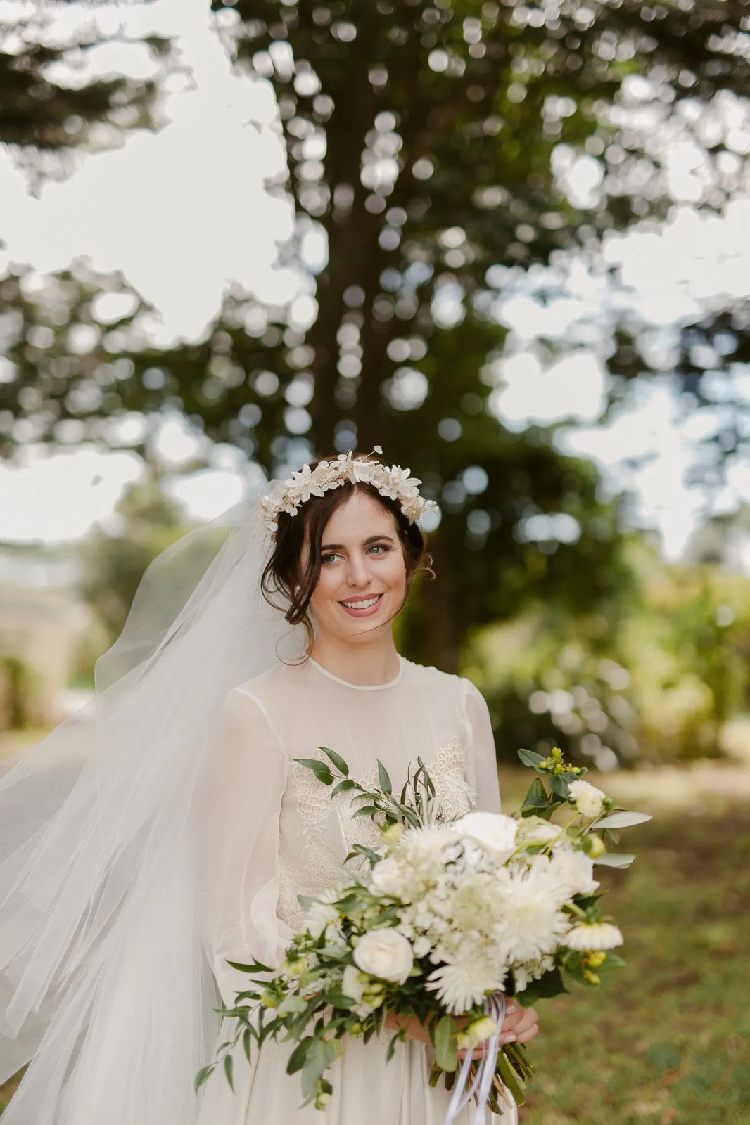 A bride in a flower crown and veil holding a white bouquet